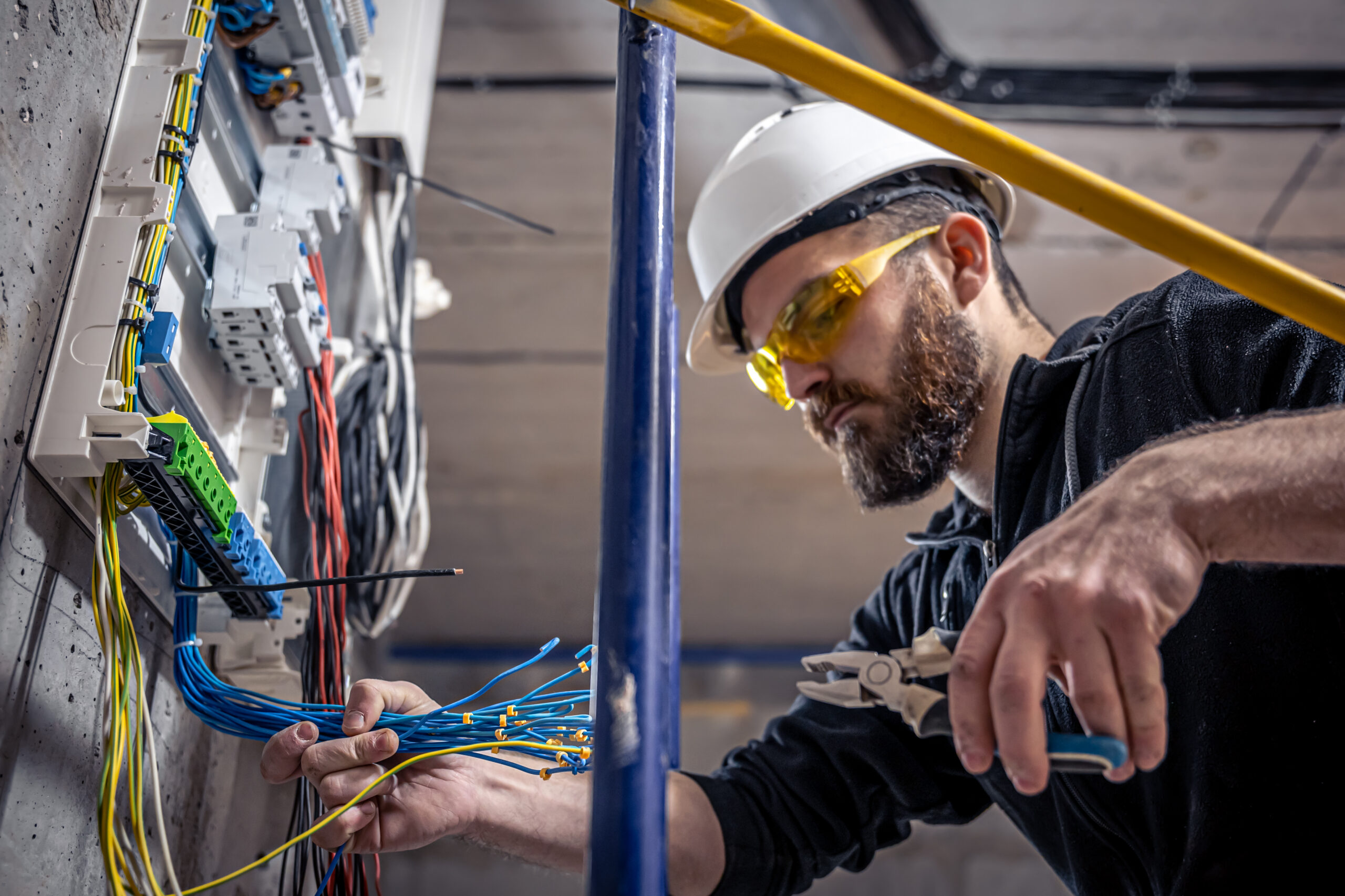 A male electrician works in a switchboard with an electrical connecting cable.